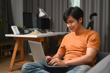 Smiling casual man sitting on sofa and using laptop computer.