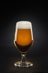 Mug with fresh beer with cap of foam on a black.