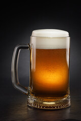 Mug with fresh beer with cap of foam on a black.