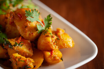 Macro Close-up of Indian vegetarian dish of spicy Potato and Tomato curry garnished with green coriander fresh leaves. 