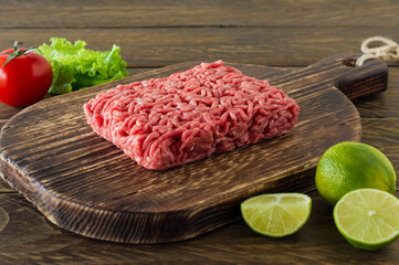 Raw minced beef meat on a wooden cutting board with vegetables and spices. Cooking and healthy eating concept.