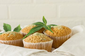 Healthy and tasty vegan and gluten free muffins topped with hemp seeds on a white plate on wooden table. Marijuana cupcake muffins with cannabis leaves