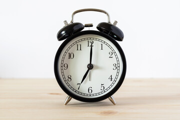 Classic black alarm clock on wooden table with white background and copy space