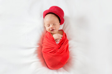 Sleeping newborn boy in a red top hat with a smile on his face. Beautiful photo of a newborn in a gentleman's suit