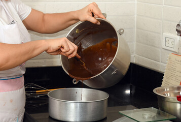 Woman cleaning chocolate residue from a steel pot with her hands.