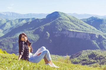 Naklejka na ściany i meble Young Woman Sitting on a Green Meadow in the Summer Mountain with Stunning View . Balkan Mountains ,Bulgaria 