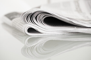 Folded newspapers mirrored on glass table against plain background with narrow depth of field