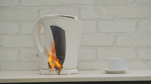 Plastic electric kettle burns with fire and melts on table in kitchen at home. Concept of cause of fire in house.
