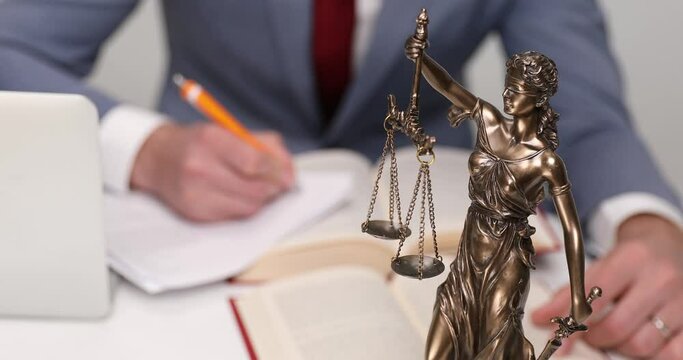 businessman writing down something at his desk, behind his balance statue