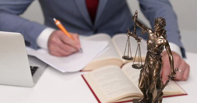desk with books and papers, laptop, libra statue and a businessman writing 