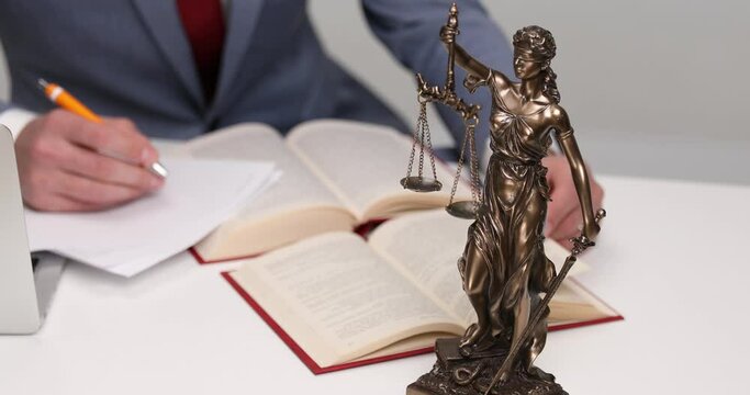 businessman at desk turning pages, writing down next to his balance statue