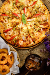 Vertical photo and close up on tasty homemade seafood pizza on sackcloth with dried flowers, cold beverage, Fried onions on wooden table. Food and Beverage Concept.