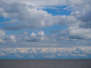 White cumulus clouds in a blue sky over a seascape, a large number of clouds over a panorama of ocean water, cloudy weather