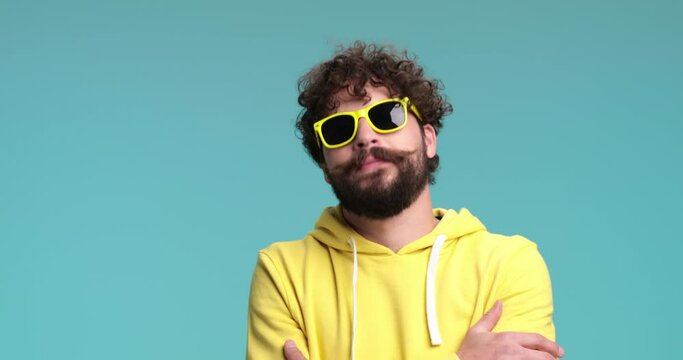 confident young hipster with long beard and moustache crossing arms and being cool, nodding, dancing, making dynamic moves with enthusiasm, having a seizure and being cool again on blue background