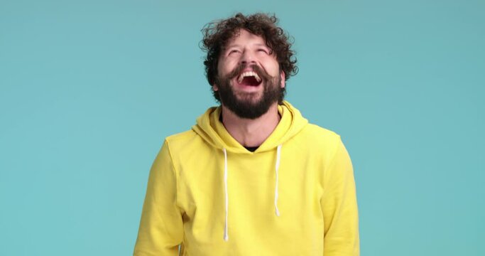 happy casual hipster guy in yellow hoodie having fun, laughing, being bipolar and becoming serious, looking to side and laughing again on blue background in studio