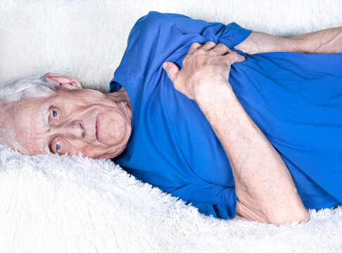 Male Hand Holding Heart. Eldery Man Laying On White Sofa And Suffering From Heartache.