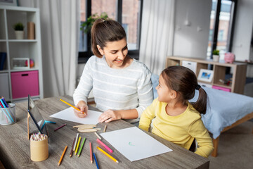 family, motherhood and leisure concept - mother spending time with her little daughter drawing with color pencils at home