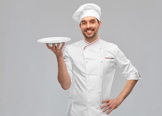 cooking, culinary and people concept - happy smiling male chef in toque holding empty plate over grey background