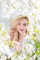 Portret beautiful young woman in a  dress with a straw hat walks in the spring garden.
