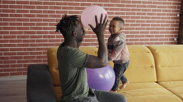 African-American father playing with cute little boy using two balloons