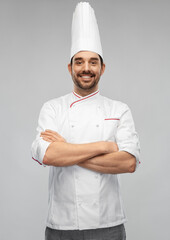 cooking, culinary and people concept - happy smiling male chef in toque and jacket with crossed arms over grey background