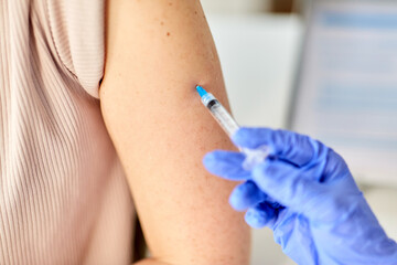 health, medicine and pandemic concept - close up of doctor or nurse with syringe vaccinating patient at hospital