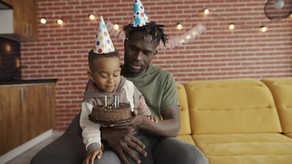 African American father holds son - blowing three candles on birthday's cake