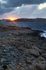 Obraz premium Glowing sunset with rays over the water on a beach in Qawra, Malta on an autumn night.