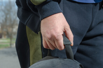 Close-up of a man's hand holding a backpack by the handle.