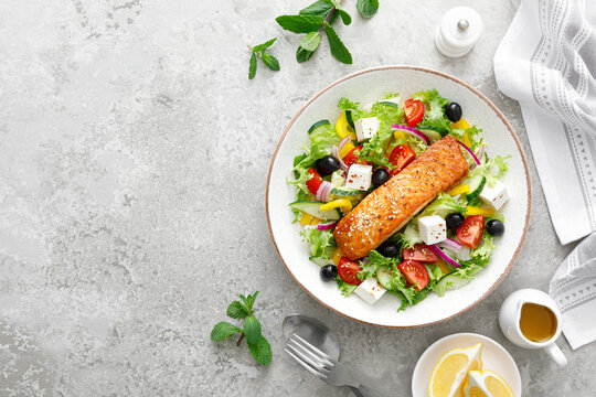 Salmon fish salad. Fresh vegetable greek salad with tomato, pepper, lettuce, olives, cucumbers, feta cheese and grilled salmon fish fillet, healthy food, omega 3, keto diet, mediterranean cusine