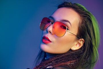 Asian girl in sunglasses and black leather jacket posing against dark blue background