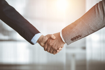 Business people standing and shaking hands in sunny office, close-up. Handshake and marketing