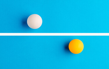 White and orange table tennis balls are opposed to each other divided by a line on blue background.