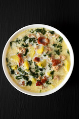 Homemade Zuppa Toscana with Kale and Bread in a white bowl on a black background, top view. Overhead, from above.
