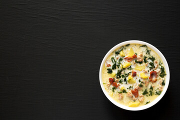 Homemade Zuppa Toscana with Kale and Bread in a white bowl on a black background, top view. Overhead, from above. Space for text.