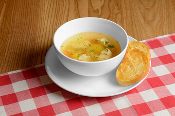 Chicken broth soup with vegetables served in a white bowl over red plaid tablecloth. Ukrainian cuisine concept.
