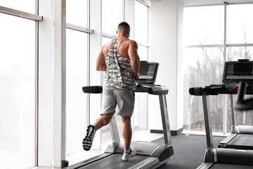 Fototapeta premium Muscular athletic bodybuilder fitness model running treadmill gym near big window