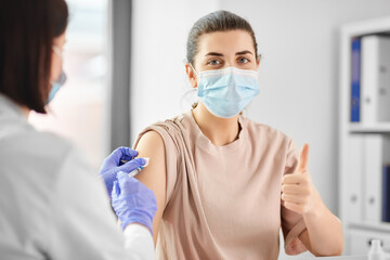 Fototapeta na wymiar health, medicine and pandemic concept - female doctor or nurse wearing protective medical mask with syringe vaccinating patient showing thumbs up at hospital