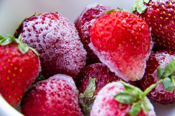 Frozen strawberries with ice on the plate. Frozen red berries.