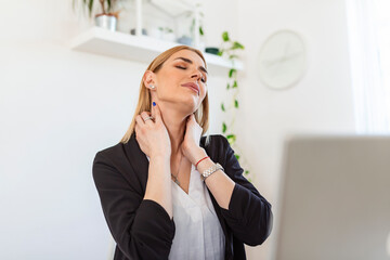 Feeling exhausted. Frustrated young woman looking exhausted and massaging her neck while sitting at her working place