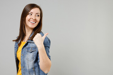 Young smiling caucasian woman 20s wear casual trendy denim jacket yellow t-shirt point thumb finger back aside on workspace copy space area mock up isolated on grey color background studio portrait