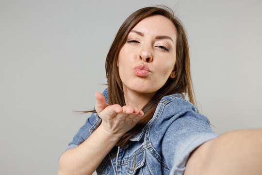 Close up young girlfriend lovely happy caucasian woman 20s wear casual denim jacket yellow t-shirt doing selfie shot on mobile phone blowing air kiss isolated on grey color background studio portrait
