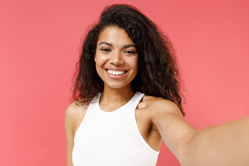 Close up young friendly happy smiling student african american woman wearing white tank shirt doing selfie shot on mobile phone isolated on pink background studio portrait. People lifestyle concept.