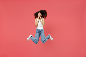 Full length young fun amazed surprised impressed happy friendly satisfied positive cute african american woman 20s wear casual white tank shirt jump high hold face scream isolated on pink background