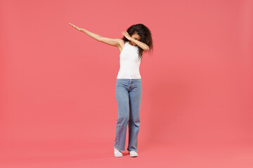 Full length young african american woman 20s wear casual white tank shirt doing dab hip hop dance hands move gesture youth sign hiding covering face isolated on pink color background studio portrait.