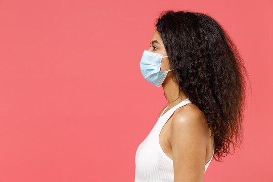 Side Profile View Young African American Woman In Casual White Tank Shirt Sterile Face Mask Ppe To Safe From Coronavirus Virus Covid-19 Flu On Lockdown Quarantine Isolated On Pink Color Background