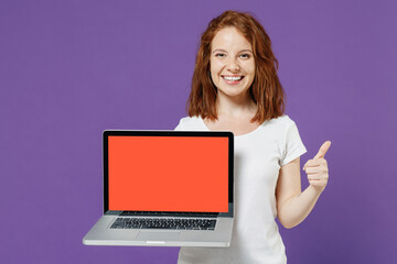 Young redhead woman 20s in white basic casual t-shirt holding using laptop pc computer with blank screen workspace area show thumb up gesture isolated on dark violet color background studio portrait