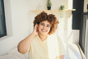 Obraz na płótnie Canvas Beautiful happy curvy plus size African black woman afro hair posing in beige t-shirt and underwear on sunny balcony bedroom. Body imperfection, body acceptance, body positive and diversity concept.