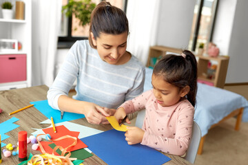 Obraz premium family, art and craft concept - mother spending time with her little daughter with glue making applique of color paper at home