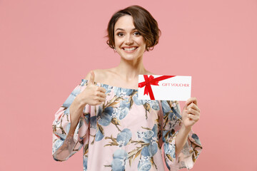 Young happy satisfied caucasian woman with short hairdo in trendy stylish blouse hold in hand gift voucher flyer mock up show thumb up like gesture isolated on pastel pink color background studio